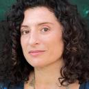 Headshot of Julia Loktev, a woman with dark curly hair, brown eyes, wearing a blue top and gold necklace.